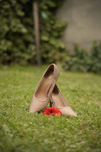Stylish high heels placed on grass with a vibrant red flower in the foreground.