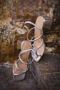 Elegant pair of silver high-heeled sandals resting on rustic stone outdoor surface.