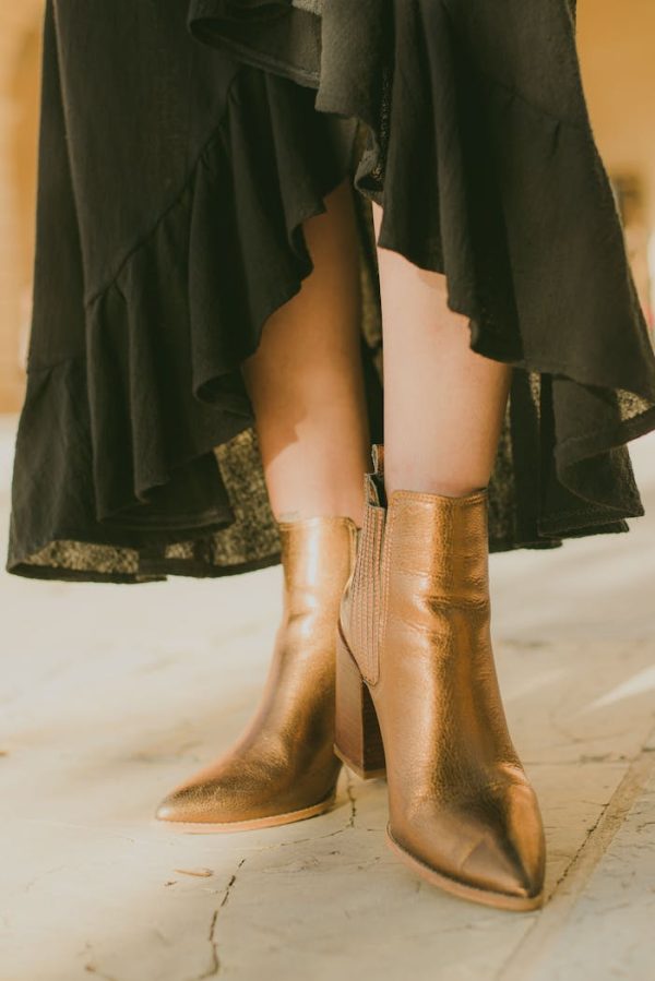 Close-up of elegant gold ankle boots and a flowing black skirt indoors.